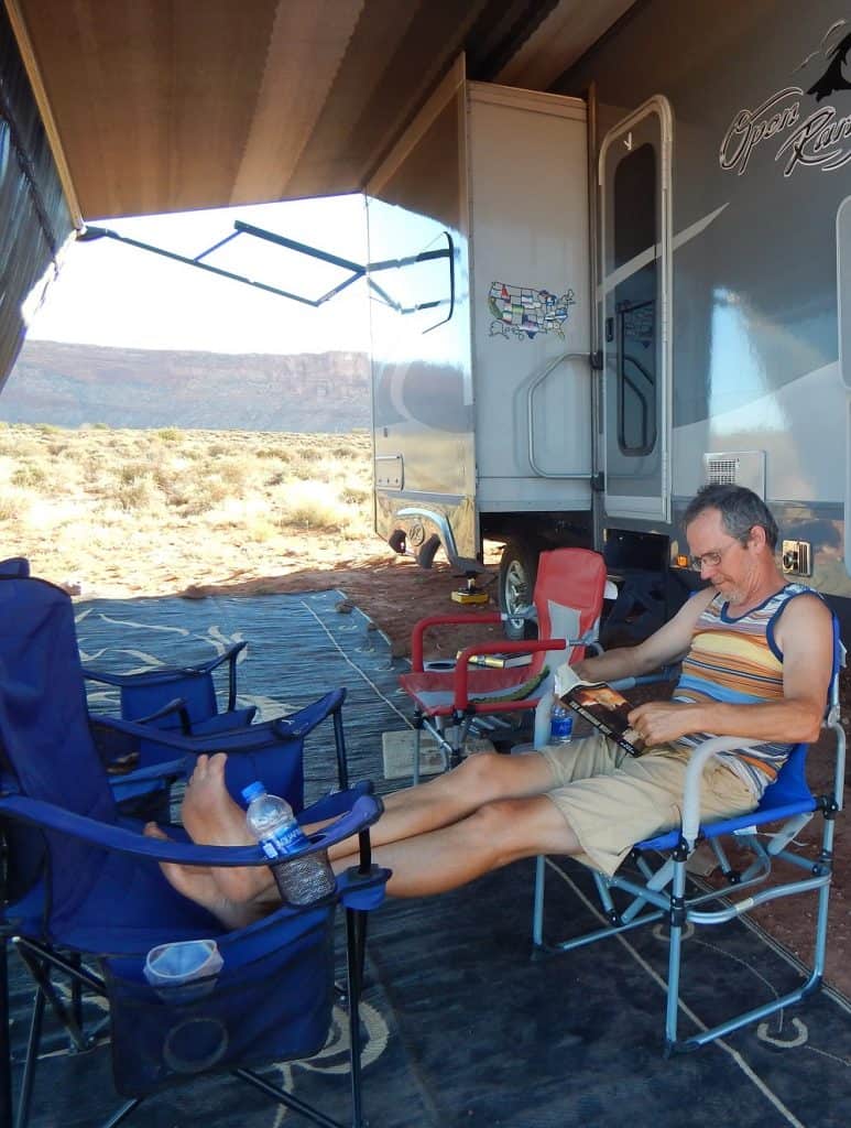 Frank sitting outside under our RV screen reading a book while RV boondocking
