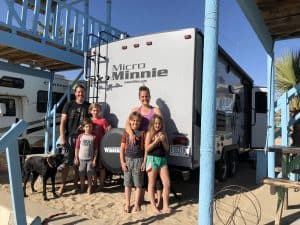 A family of 6 standing in front of their Miniie Micro RV on the beach