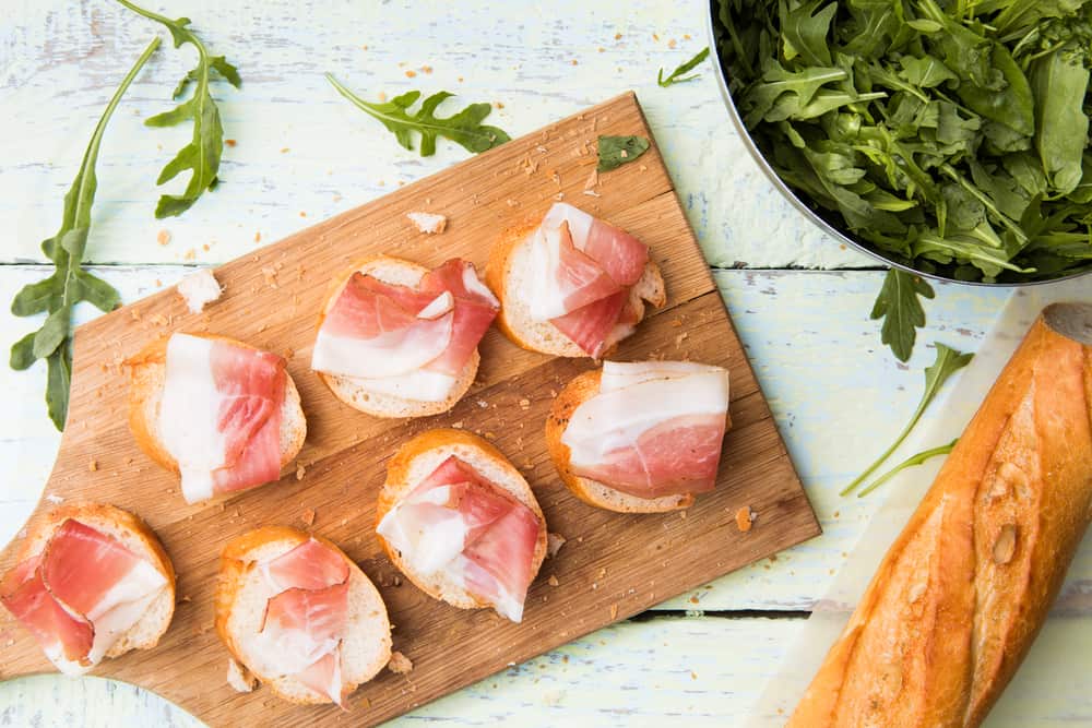 Bread with bacon on white wooden table with arugula and spices