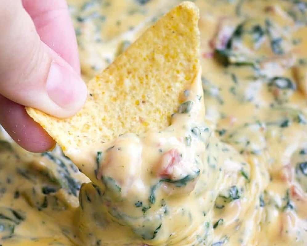 fingers holding a corn chip with queso sauce