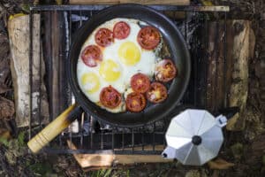 cast iron pan with eggs and tomatoes, pot of coffee over fire