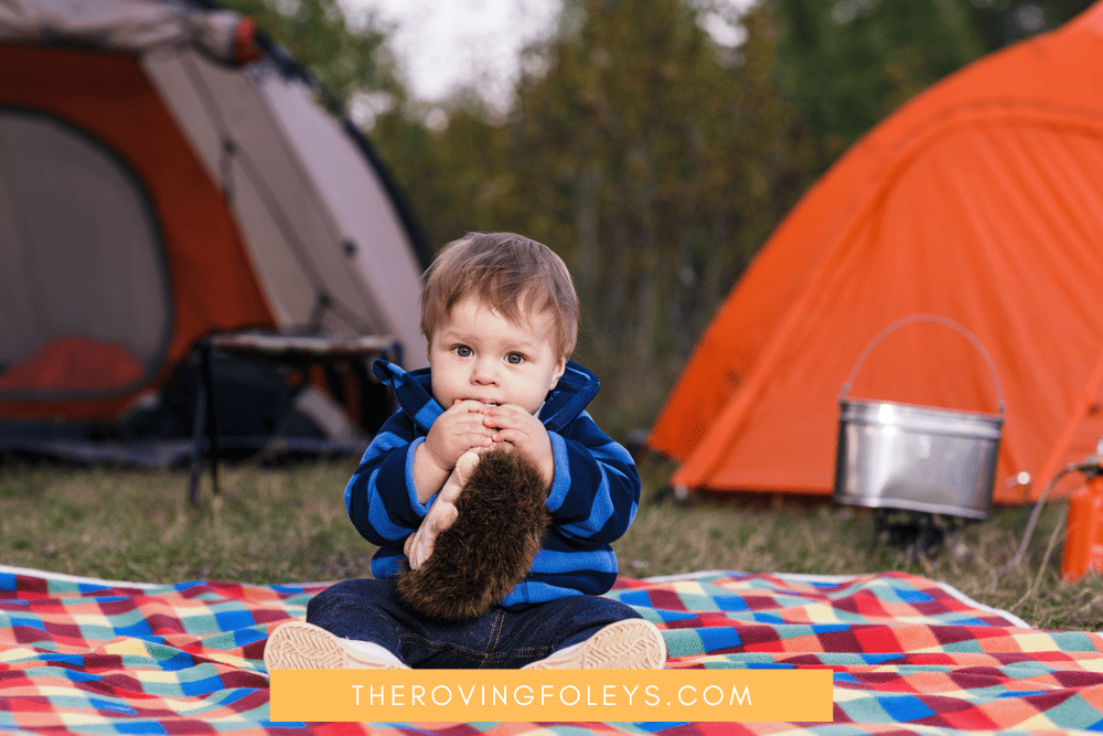 toddler boy sitting on blanket by tents