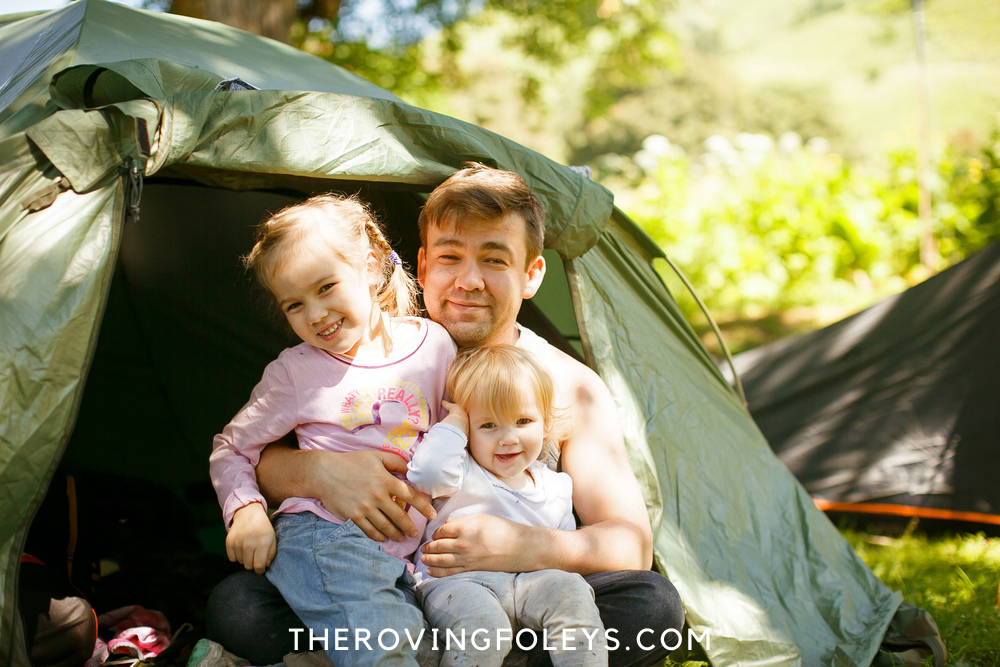 Dad holding 2 toddlers outside tent
