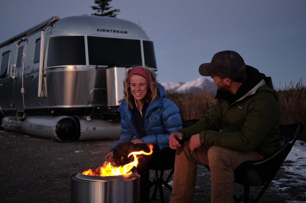 couple sitting at fire near airstream with airskirts